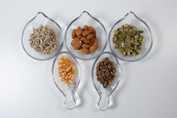 Various seeds - sunflower, almonds, pumpkin seed, corn and coffe in diferent glass bowls on a white background. Copy space.