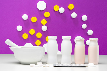 Probiotics with bifidobacteria. Multicolored pills on pink background. Bowl for grinding medicines. White bottles on table. Cooking yogurt with bifidobacteria. Making probiotics. Probiotics bacteria