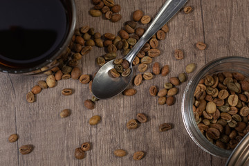 glass cup with black coffee, jar with seeds, a spoon and coffee seeds on a wooden board.