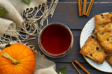 Autumn flatlay with pumpkin, cookies, clay cup with tea and cinnamon chopsticks on gray wooden background.
