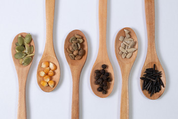 Different seeds -maize, squash, coffee, pepper, rice, sunflower- in wooden spoons on a white surface