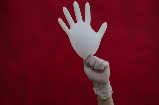 Hand Holds Inflated Medical Glove On A Red Background