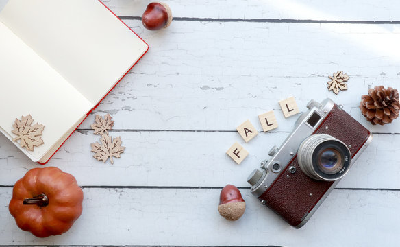 top view of fall-themed elements on a rustic wood surface: vintage camera, open notebook, letters, pumpkin, pinecones, acorns and a scarf with copy space.  diagonal arrangement
