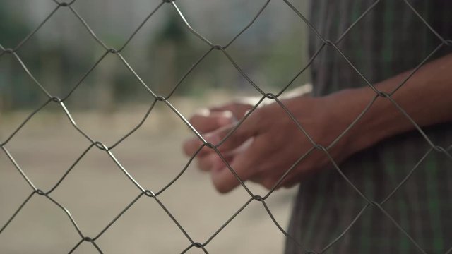 Close-up of male African American and Caucasian hands passing money and pills through mesh fence. Unrecognizable dealer and narcomaniac exchanging outdoors at sunset. Drug addiction, criminality.