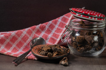 Jar with mushrooms, a dish towel and dried pine mushrooms in a small plate on a table