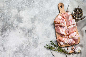 Bacon with pepper and thyme on a chopping Board. Organic raw pork meat. Gray background. Top view. Copy space