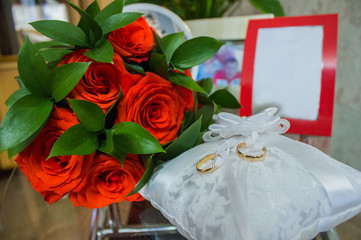 Composition of wedding accessories on the table. Red roses and rings of the bride and groom.
