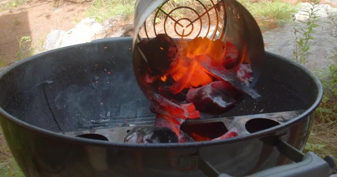 Burning red hot charcoal lumps being dumped out of a charcoal chimney starter into a kettle grill