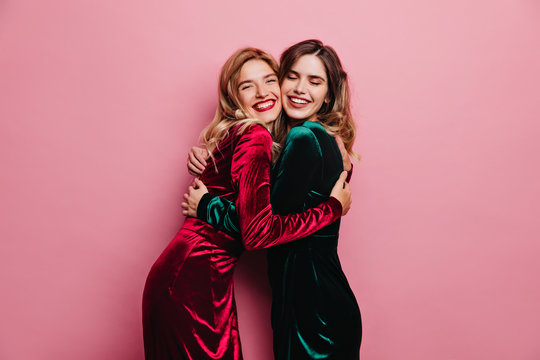 Excited female friends huggs on pink background. Indoor photo of blithesome adult sisters posing with smile.