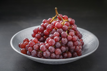 fresh red grape in nice metal plate on dark gray, grey, black tone texture background