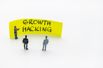 Presentation meeting with miniature figurines posed as business people standing in front of post-it note with Growth Hacking handwritten message in background, copy space on the right