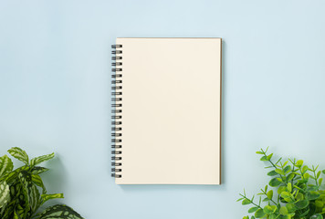 Spiral Notebook or Spring Notebook in Unlined Type and Office Plants at Bottom on Blue Pastel Minimalist Background