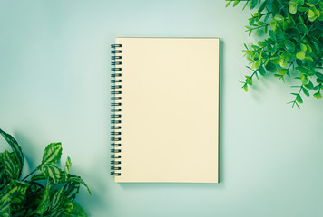 Spiral Notebook or Spring Notebook in Unlined Type and Office Plants at Top Right Corner and Bottom Left Corner on Blue Pastel Minimalist Background in Vintage Tone