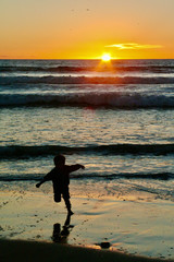 Silhouette of a Dancing Child playing on the beach at sunset with rays of sun reflecting on the ocean