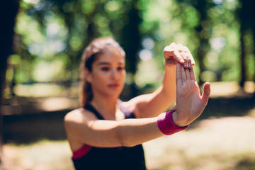 Closeup of gorgeous female runner standing in woods and stretching hand before exercising.