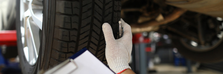 Close-up of mechanic writing on clipboard white examining car wheel. Inspector with tablet checking automobile before driving. Repair service station and maintenance concept © H_Ko