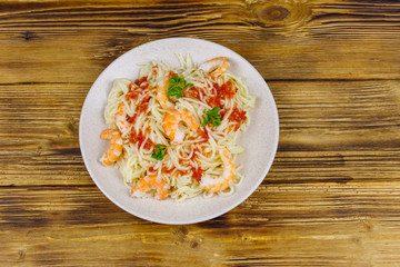 Spaghetti pasta with prawns, tomato sauce and parsley on wooden table. Top view