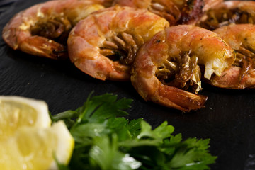Large oceanic shrimps fried with lemon and parsley on a black stone board. Sea food.