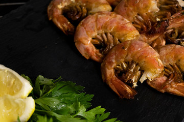 Large oceanic shrimps fried with lemon and parsley on a black stone board. Sea food.