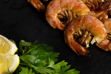 Large oceanic shrimps fried with lemon and parsley on a black stone board. Sea food.