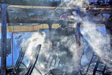 firefighter putting out fire in a totally burned bus.