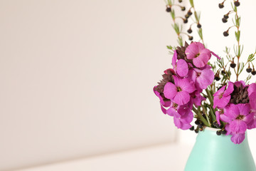 Basic white background image featuring purple wallflowers and boronia stems in small green vase with copy space