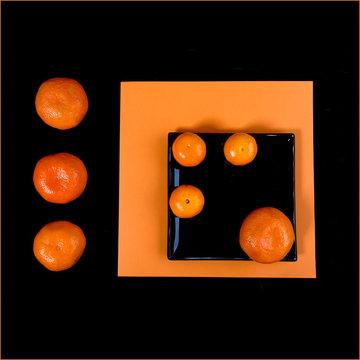 Composition Of Orange Mandarin And Black Square Plate On An Orange Table.