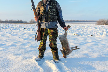 A hunter with a gun holds in his hands the prey of a hare.