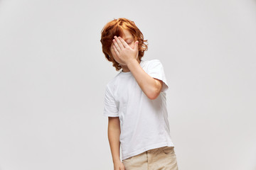 Red-haired boy mortgage near face in white t-shirt gray background 