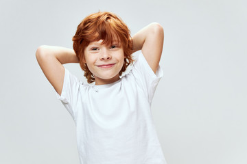 Red-haired boy holds hands behind his head smile white t-shirt studio