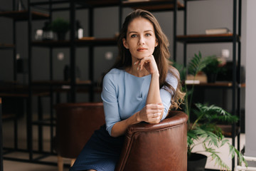 Beautiful young businesswoman wearing stylish light blue dress sitting at the chair in office with...
