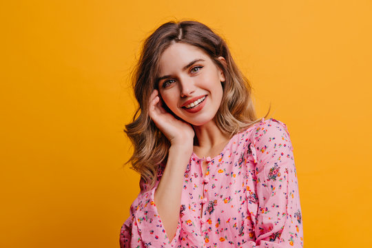 Cute beautiful woman with wavy hair laughing on yellow background. Indoor photo of pretty white girl wears pink blouse.