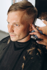  A blond hair man is hair cutting with barber in the barbershop. Haircut with an electric razor. Self-care. Close-up haircut. High quality photo