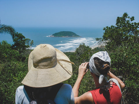 Two unrecognizable young women look towards Praia da Barra de Ibiraquera, Imbituba, Brazil. Concept of tourism.