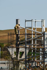 Worker is working at a construction site while on scaffolding. Workers are welding. Metal construction.