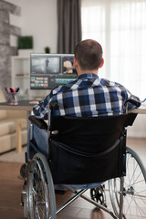 Disabled video editor sitting on wheelchair doing post production on film. Invalid videographer doing his business online, using high technology, sitting in his apartment, working remotely in special