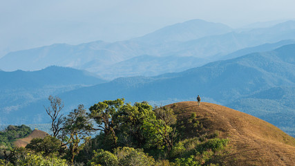 Backpacker standing on the mountain peak looking out to the mountain range scenic view