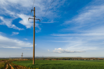Obraz premium A row of poles of a power line in a field near a dirt road under a clear sky. Electricity transmission line, power supply