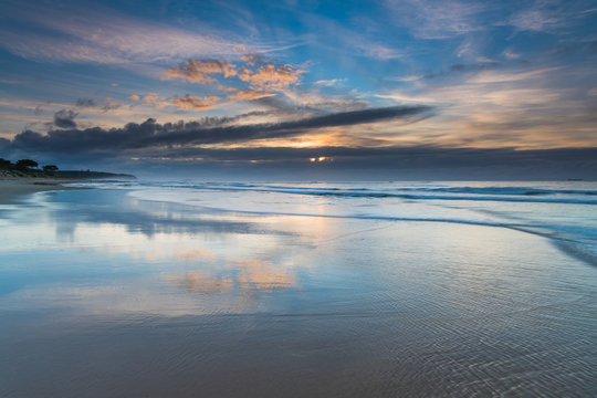 Sunrise Seascape with Clouds and Reflections on the Beach