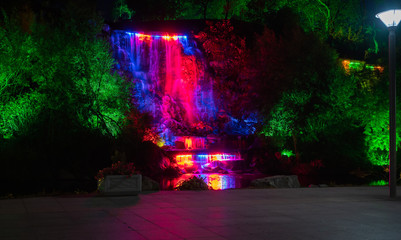 Night landscape, falling fountain with multi-colored paints a public park