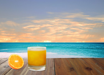 a glass of orange juice and a slice orange fruit are on the wooden table near the beach with background of blue sky in the summer holidays (clipping path included)