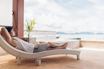 Asian man is lying on the bench feeling relax with the sea view on his vacation.
