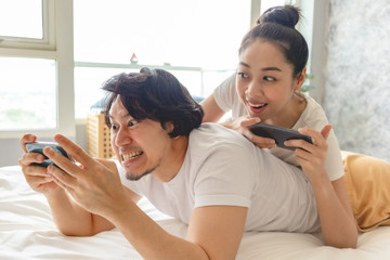 Excited Asian couple is playing mobile phone together in their apartment.