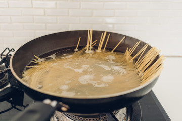 Image of boiling spaghetti with the pan in white kitchen.