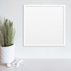 White frame mockup on white wall with beach/ocean theme decoration on white surface. Copy space.