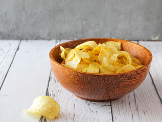 Potato chips or crisps in wooden bowl against white wooden background. Pile of potato chips. Potato chips is snack. Top view