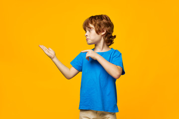 redheaded boy blue t-shirt yellow background freckles and point your hand to the side to the free space
