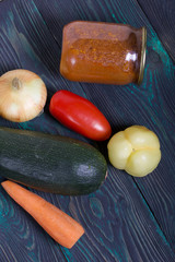 Canned zucchini caviar in a jar. Nearby on the table surface are vegetables, ingredients for cooking.