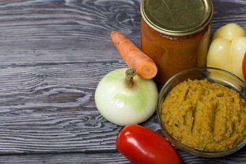 Freshly prepared zucchini caviar in a container. Next to it, canned zucchini caviar in a jar. On the surface of the table vegetables, ingredients for cooking.