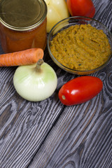 Freshly prepared zucchini caviar in a container. Next to it, canned zucchini caviar in a jar. On the surface of the table vegetables, ingredients for cooking.